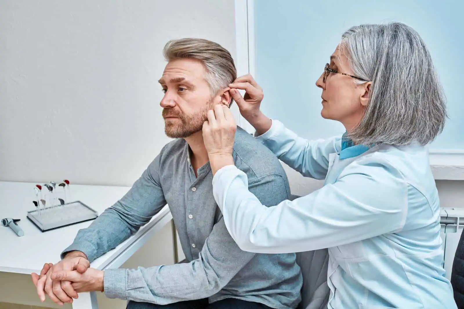Female audiologist fitting hearing aid on patient