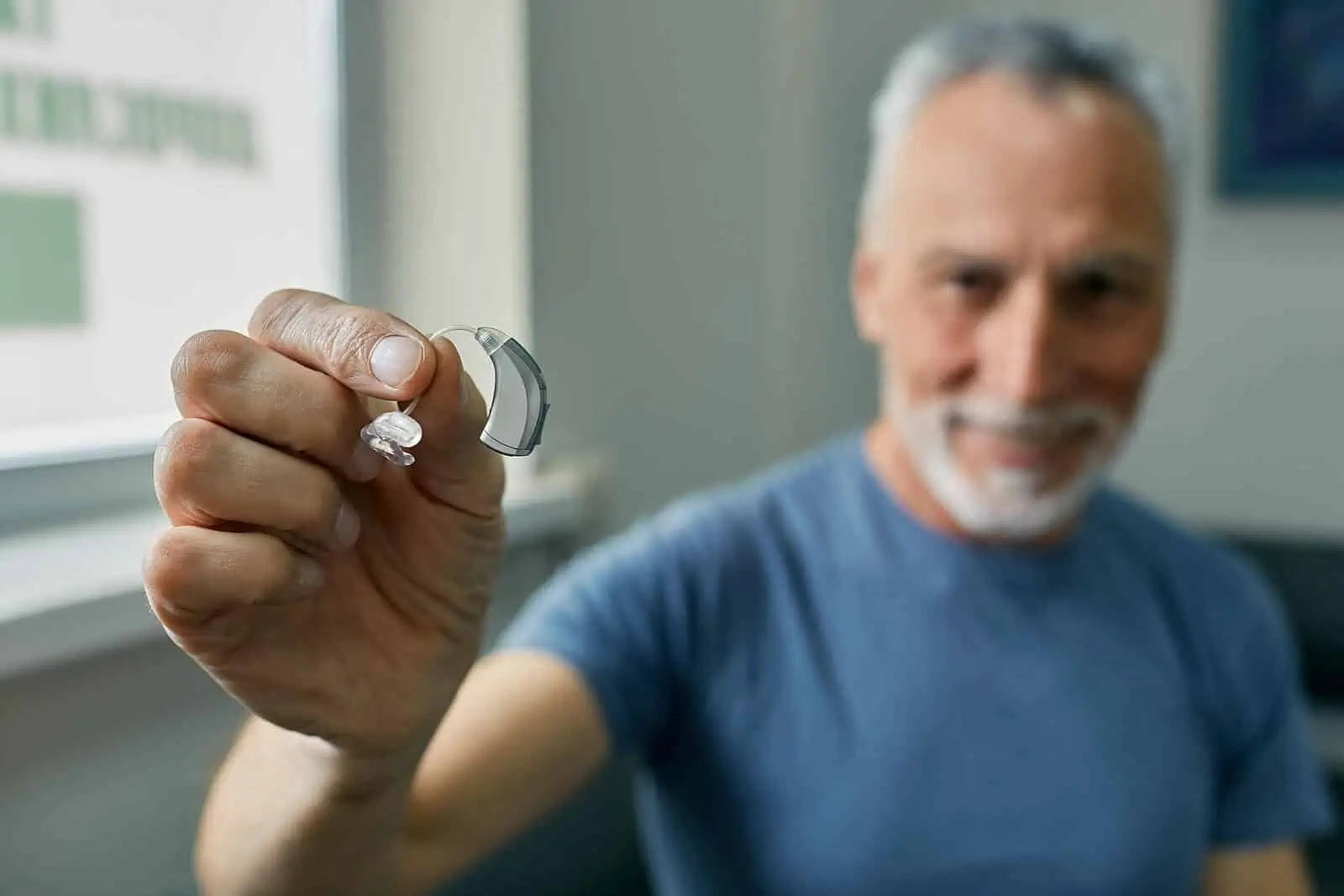 Elderly man holding up a BTE hearing aid