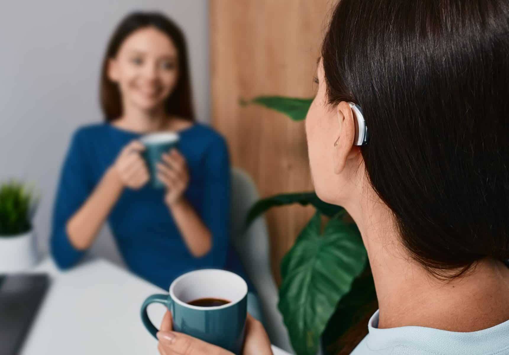 Woman with hearing aid having coffee and conversation with another woman