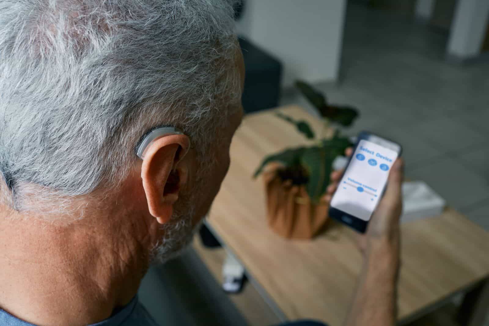 Senior man with hearing aids adjusting volume with phone app